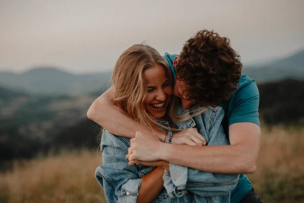 Jovem casal em um passeio na natureza ao pôr do sol no campo, abraçando e se divertindo. — Fotografia de Stock