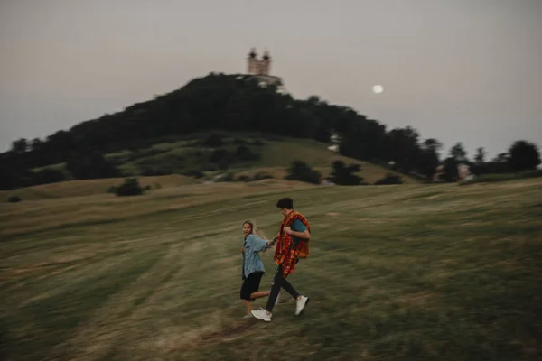 Genç çift gün batımında doğada yürüyor kırsalda, el ele tutuşuyorlar ve koşuyorlar.. — Stok fotoğraf