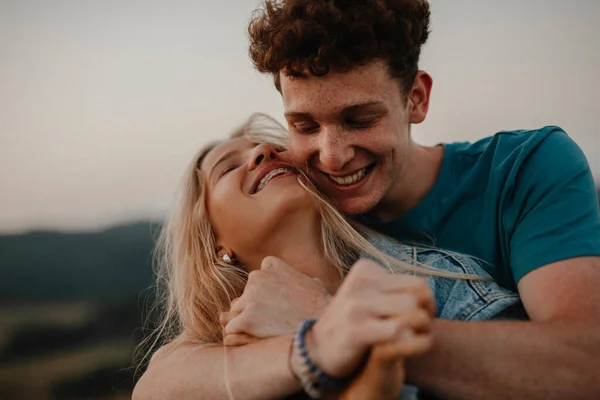 Pareja joven en un paseo por la naturaleza al atardecer en el campo, abrazándose y divirtiéndose. — Foto de Stock