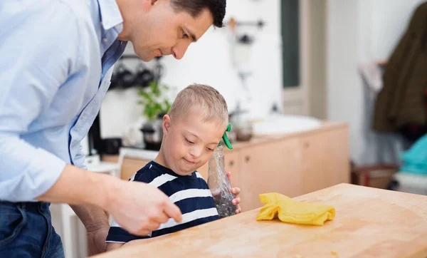 Pai com feliz síndrome de down filho dentro de casa na cozinha, mesa de limpeza. — Fotografia de Stock