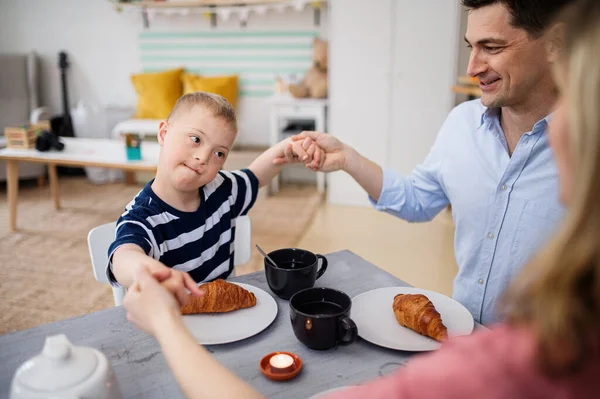 Happy down syndrome boy with parents at the table, praying before breakfast. — Stock Photo, Image