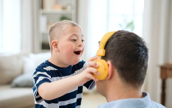 Happy Down syndroom jongen met vader binnen thuis, plezier hebben met koptelefoon. — Stockfoto
