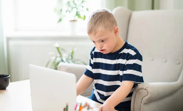 Down syndrome boy indoors at home, using laptop. — Stok Foto