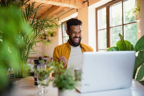 Vrolijke jongeman met laptop die binnen werkt, home office concept. — Stockfoto