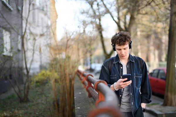 Portrét mladého muže dojíždějícího do práce se sluchátky procházejícími venku ve městě, pomocí smartphonu. — Stock fotografie