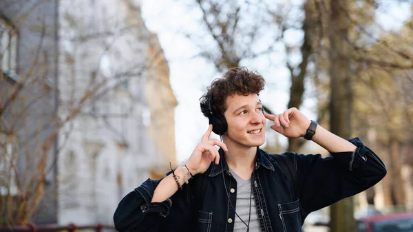 Portrait de jeune homme banlieusard avec écouteurs marchant à l'extérieur en ville, écoutant de la musique. — Photo