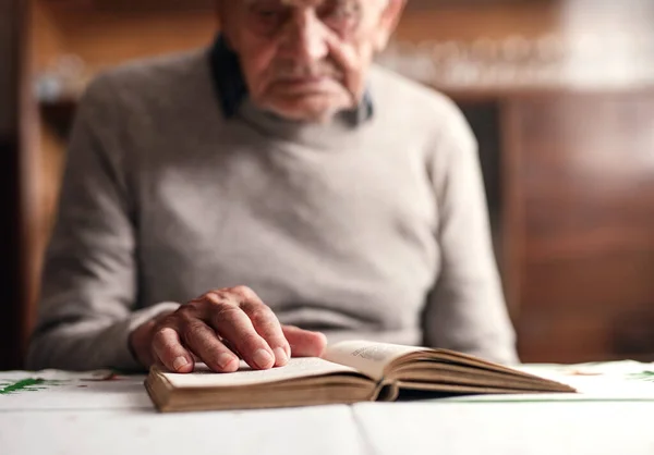 Porträtt av äldre man sitter vid bordet inomhus, vila och läsa bibeln. — Stockfoto