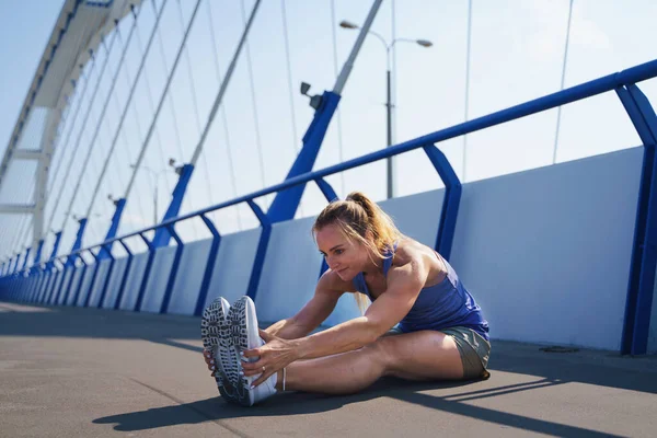 Média mulher adulta corredor que se estende ao ar livre na ponte na cidade, conceito de estilo de vida saudável. — Fotografia de Stock