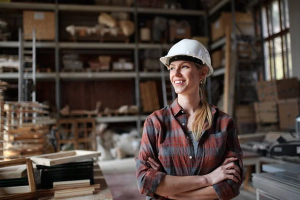 Retrato de carpinteiro feminino adulto médio em pé na oficina de carpintaria, olhando para o lado e sorrindo. Conceito de pequenas empresas. — Fotografia de Stock