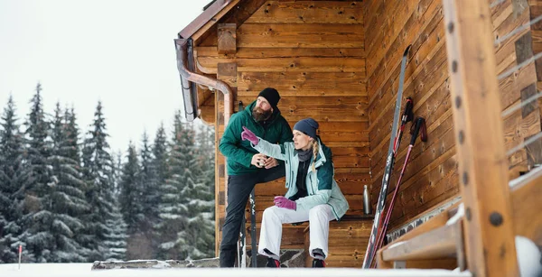 Mature couple resting by wooden hut outdoors in winter nature, cross country skiing. — Stock Photo, Image