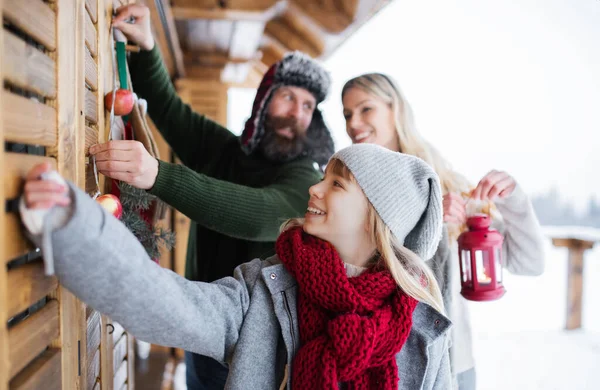 Familia con pequeña hija decorando terraza de la casa al aire libre en invierno, tiempo de Navidad. — Foto de Stock