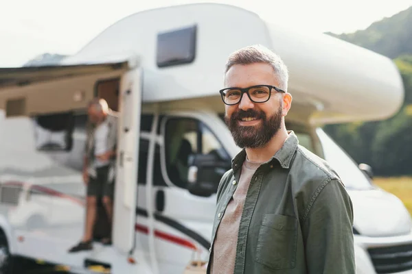 Portrait of happy man standing by car outdoors in campsite, looking at camera. Caravan family holiday trip. — Stock Photo, Image