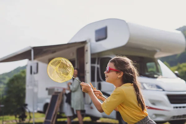 Feliz niña pequeña de pie al aire libre con red de mariposas en coche caravana, viaje de vacaciones en familia. — Foto de Stock