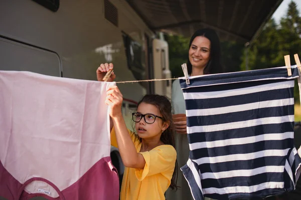 Mother with daughter hanging clothes by car outdoors in campsite, caravan family holiday trip. — Stock Photo, Image