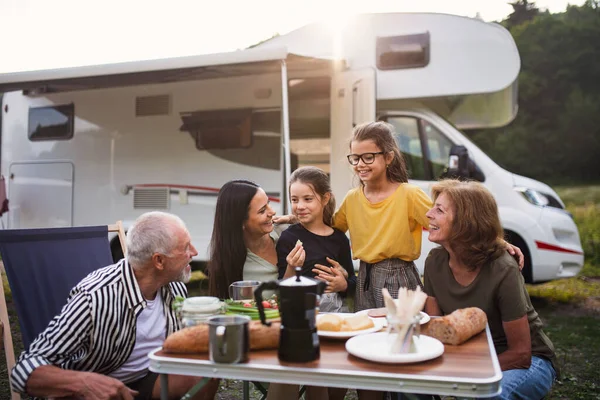 Multi-generation family sitting and eating outdoors by car, caravan holiday trip. — Stock Photo, Image