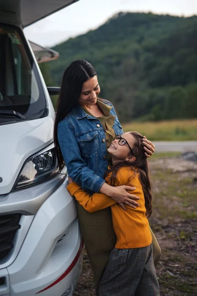 Mãe com a filha pequena abraçando de carro ao ar livre no acampamento ao entardecer, viagem de férias em família caravana. — Fotografia de Stock