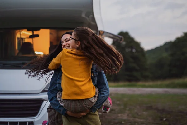 快乐的母亲和小女儿在黄昏的时候，在露营地，在大篷车的家庭假日旅行中，开车拥抱在一起. — 图库照片