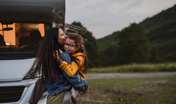 Mãe feliz com a filha pequena abraçando de carro ao ar livre no acampamento ao entardecer, viagem de férias em família caravana. — Fotografia de Stock
