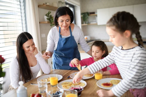 Niñas felices con madre y abuela comiendo panqueques en casa, almorzando. —  Fotos de Stock