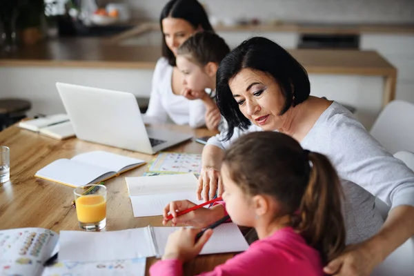 Felice ragazze piccole con la madre e la nonna facendo i compiti utilizzando il computer portatile in casa, home office e homeschool concetto. — Foto Stock