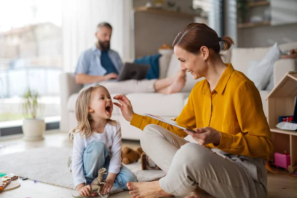 Mor med liten datter som leker og jobber innendørs, hverdagsliv og hjemmekontor med barnekonseptet. – stockfoto