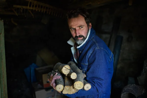Portret biednego dojrzałego mężczyzny trzymającego drewno na opał w domu, patrzącego w kamerę, koncepcja ubóstwa. — Zdjęcie stockowe