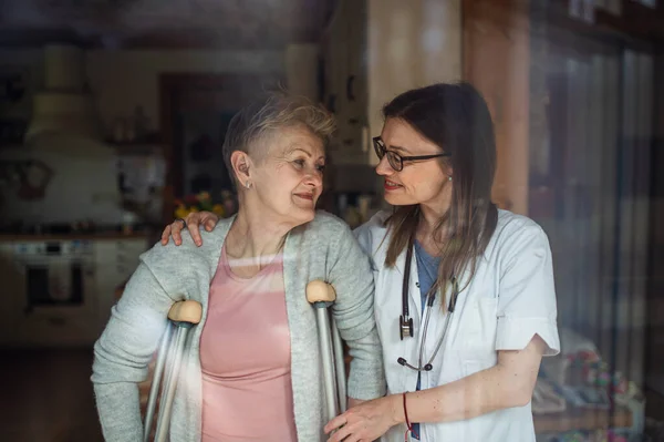 Hälso- och sjukvårdspersonal eller vårdgivare besöker äldre kvinna inomhus, hjälper henne att gå. — Stockfoto