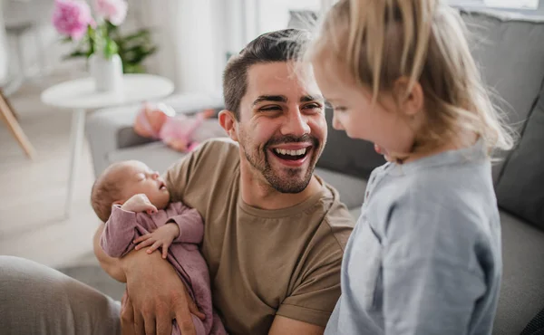 Joyeux jeune homme prenant soin de son nouveau-né et de sa petite fille à l'intérieur à la maison, congé de paternité. — Photo