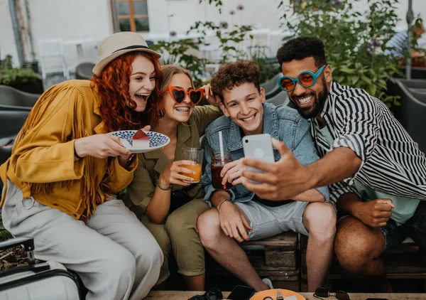 Grupo de jovens felizes com smartphone sentado no café ao ar livre na viagem à cidade, tirando selfie. — Fotografia de Stock