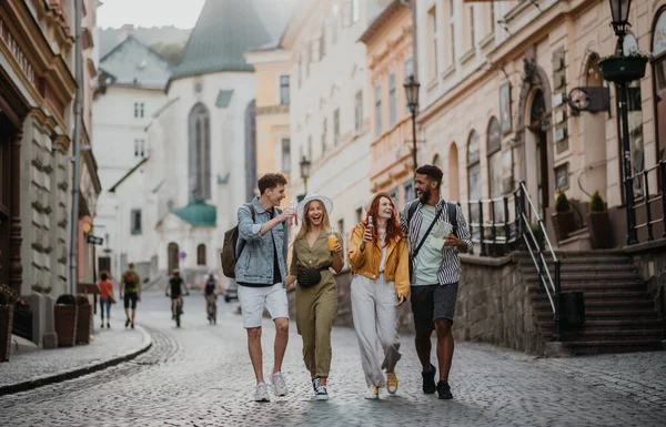 Front view of group of happy young people with drinks outdoors on street on town trip, laughing. — Stock Photo, Image