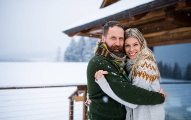 Mutlu yetişkin bir çiftin dağ kulübesinde birbirlerine sarılıp tatilin tadını çıkarırken çekilmiş bir portresi..