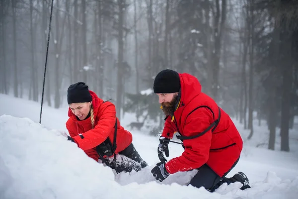 Górski ratowniczy służba na praca na zewnątrz w zimie w las, kopanie śnieg z łopata. — Zdjęcie stockowe