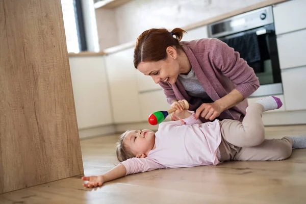 Mãe feliz com a filha pequena brincando dentro de casa na cozinha, rindo. — Fotografia de Stock