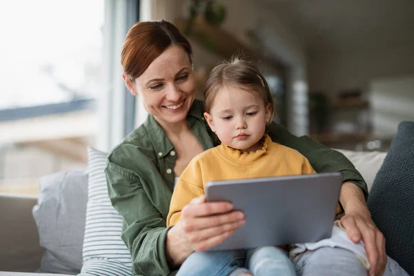 Glückliche Mutter mit kleiner Tochter schaut zu Hause Kinderprogramm auf dem Tablet, Alleinerziehendes Konzept. — Stockfoto
