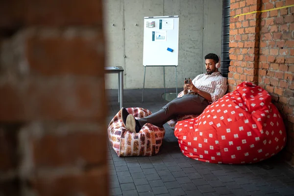 Giovane uomo d'affari con smartphone e cuffie prendersi una pausa in ufficio, a riposo. — Foto Stock