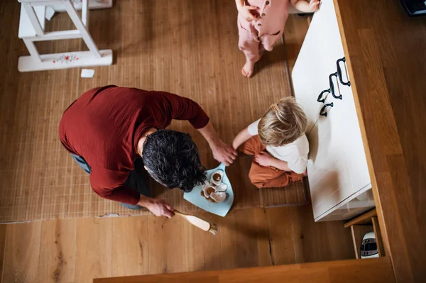 Blick von oben auf Vater mit kleinen Kindern, der zu Hause Scherben fegt, Konzept der täglichen Hausarbeit. — Stockfoto