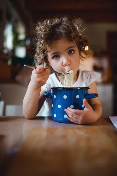 Niña triste sentada en la mesa en casa, comiendo espaguetis. — Foto de Stock