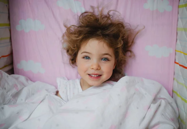 Ovanifrån av glad liten flicka ligger i sängen inomhus — Stockfoto