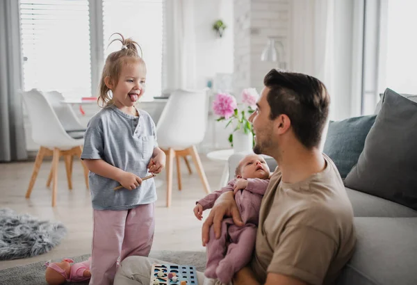 Feliz joven cuidando a su bebé recién nacido y a su pequeña hija en casa, licencia de paternidad. — Foto de Stock