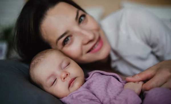 Вид спереду щасливої молодої матері зі своєю новонародженою дівчинкою, що лежить на дивані вдома, дивлячись на камеру . — стокове фото