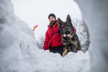Köpeğiyle birlikte kışın ormanda kar kazan dağ kurtarma ekibinin düşük açılı görüntüsü..
