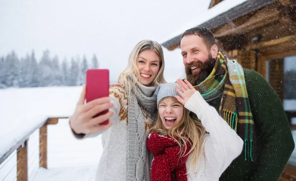 Щаслива сім'я з маленькою донькою, яка приймає селфі на гірській хатинці на відкритому повітрі взимку . — стокове фото