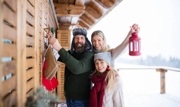 Familj med liten dotter dekorera terrass hus utomhus på vintern, juletid, tittar på kameran. — Stockfoto