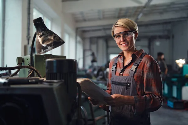 Porträtt av en medelvuxen industrikvinna som arbetar inomhus i en metallverkstad och tittar på kameran. — Stockfoto