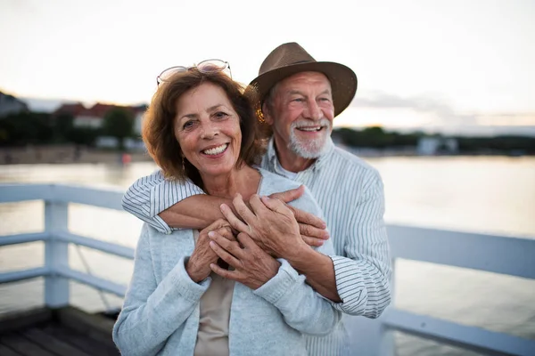 Glada äldre par kramas utomhus på piren vid havet, tittar på kameran. — Stockfoto