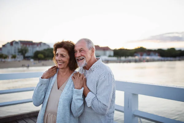 Heureux couple de personnes âgées étreignant à l'extérieur sur la jetée par la mer, en regardant la vue. — Photo