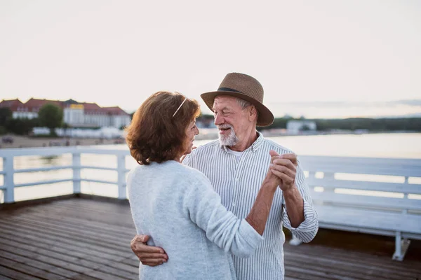 Happy senior couple dancing outdoors on pier by sea, looking at each other. — Stock Photo, Image