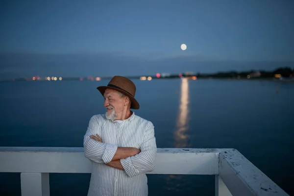 Portret van een oudere toerist die buiten op de pier aan zee kijkt. — Stockfoto