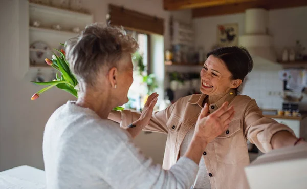 Volwassen dochter op bezoek bij gelukkige oudere moeder thuis, moederdag of verjaardagsfeest. — Stockfoto