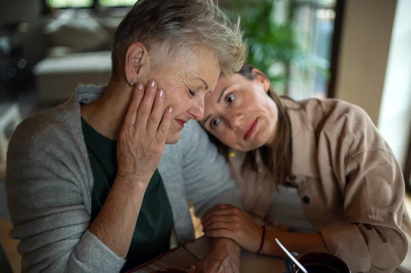 Portrait of sad senior mother with adult daughter indoors at home, hugging. — Stock Photo, Image
